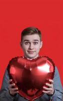 A young boy is holding and red heart shape balloon on red background representing Valentines Day photo
