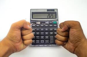 A close up of two clenched fists on either side of a calculator displaying the year 2025. This image symbolizes determination and focus on future goals photo