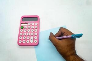A person is using a pink calculator and writing on a blue piece of paper. This image is ideal for illustrating concepts of calculation, finance, or education photo
