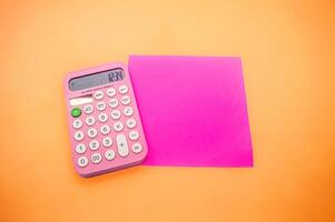 A pink calculator displaying the number 1234 is placed next to a bright pink square paper on an orange background. The vibrant colors make the image visually appealing photo