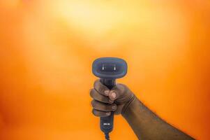 A hand holding a barcode scanner against an orange background, highlighting the device s ergonomic design and functionality. Ideal for retail, inventory, or point of sale applications photo