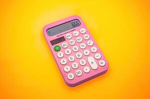 A pink calculator with white buttons on a vibrant yellow background. The display shows the number 666, making it a visually striking and colorful image photo