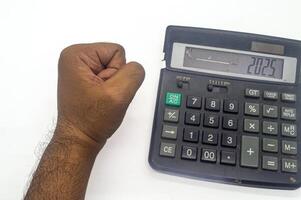 A hand forming a fist is placed next to a calculator displaying the number 2025, symbolizing financial goals or future planning photo