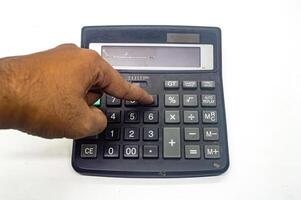 A hand pressing a button on a black calculator, highlighting the concept of finance, accounting, or mathematics. The calculator has various function keys and a large display screen photo