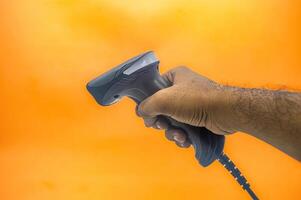 A hand holding a barcode scanner against an orange background, highlighting the device s ergonomic design and functionality. Ideal for retail, inventory, or point of sale applications photo