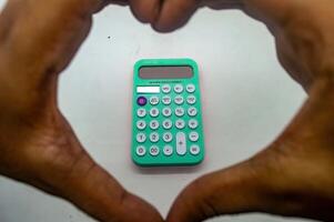 Hands forming a heart shape around a green calculator on a white background, symbolizing love for mathematics and calculations photo