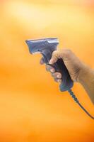 A hand holding a barcode scanner against an orange background, showcasing its ergonomic design and functionality. Perfect for retail, inventory management, and point of sale applications photo
