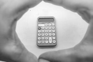 A black and white photo of a calculator framed by hands forming a circle. The calculator displays various buttons and functions, emphasizing its utility in calculations