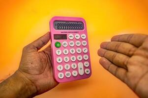 A person hand holding a pink calculator against a yellow background. The calculator displays a series of zeros and has various function buttons, making it ideal for educational or office settings photo