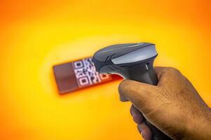 A hand holding a barcode scanner, scanning a QR code on a smartphone against a vibrant orange background, illustrating modern technology in action photo