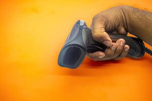 A hand holding a barcode scanner against an orange background, showcasing the device s ergonomic design and efficiency. Ideal for use in retail, inventory management, and point of sale applications photo