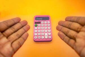 A pink calculator displaying 1000000 on its screen is held between two hands against a vibrant yellow orange background photo