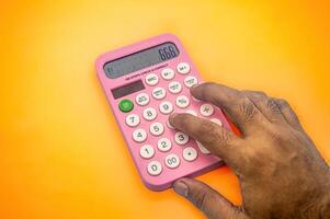 A hand using a pink calculator on a vibrant orange background. The calculator displays the number 666, making it visually striking and interesting for finance or education themes photo