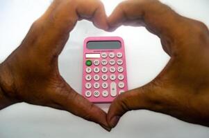 Hands forming a heart shape around a pink calculator on a white background, symbolizing love for mathematics or finance photo