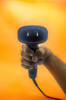 A hand holding a barcode scanner against an orange background, highlighting the device s ergonomic design and functionality. Ideal for retail, inventory, or point of sale applications photo