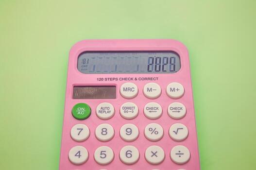 A pink calculator with a green ON or AC button on a light green background. The display shows the number 2025 and various function buttons are visible. Ideal for school or office use photo