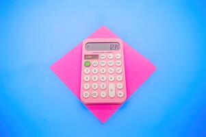 A pink calculator displaying the number 1234 is placed on a pink square paper against a blue background. The vibrant colors make it visually appealing and eye catching photo