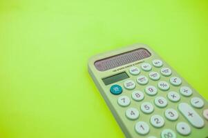 A green calculator with a large display and multiple function buttons is placed on a bright green background photo