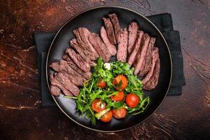 Grilled and sliced Beef Denver strip Steak on a plate with salad. brown background. top view photo