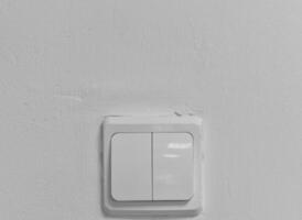 There is an electric switch on the wall. A white wall with a light switch. photo