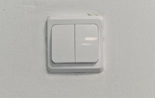 There is an electric switch on the wall. A white wall with a light switch. photo