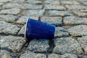 Blue plastic cup rests on cobblestone surface with greenery peeking through during daylight photo