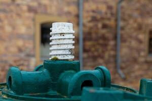 Detailed view of an old green valve with a white threaded cap in a rustic setting photo