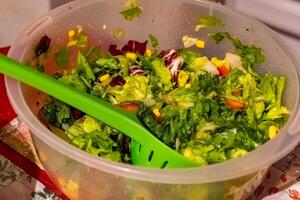 Fresh and colorful salad in a large bowl with green serving utensils at a kitchen counter photo