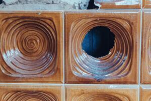 Wall tiles with swirl patterns and a hole exposed, showcasing wear and damage in an old building renovation photo