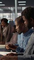 Vertical African american team examines monthly revenue balance on a computer, planning next steps in financial operations to ensure fruitful investment. Workers reviewing performance metrics. Camera B. video