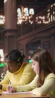 Vertical Diverse scholars helping each other finish the homework at the library, staying after classes to solve their school assignment. Clever diligent girls working hard for a scholarship. Camera A. video