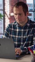 Freelancer in home office sitting at desk in front of laptop, answering phone call. Remote employee using notebook to do job online, receiving telephone call on smartphone, camera A video