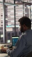 Vertical African american company worker taking a break to stretch his back in the office, trying to relieve pain after working with an uncomfortable chair and an incorrect posture. Inflammation. Camera B. video