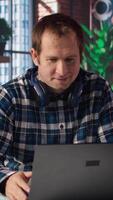 Man enjoying leisure time at home, texting friends on laptop, enjoying leisure time. Cheerful teleworker taking break to talk with mates on social network online website, using notebook, camera A video