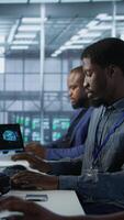Vertical Team of engineers in data center developing and maintaining disaster recovery plans ensuring minimal downtime. Server room workers using data analytics to monitor performance, camera A video
