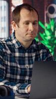 Man seated at home office desk using laptop, answering phone call while checking emails displayed on screen. Worker in telephone call with friend at work while reading messages in inbox, camera B video