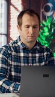 Employee completing spreadsheets on laptop and listening music. Worker in home office wearing headphones editing documents on notebook, updating reports and files, camera B video