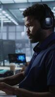 Vertical Engineer in data center wearing headphones, implementing AI systems. Server farm expert at desk in office listening music and using artificial intelligence to prevent system failures video