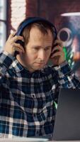 Worker listening music, analyzing data on laptop at desk, compiling analytical reports. Employee wearing headphones, using notebook device, writing down information, camera B video