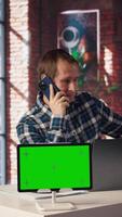 Green screen tablet next to man using laptop, answering phone call while checking emails displayed on screen. Mockup device next to worker in telephone call with friend at work, camera A video
