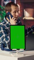 Chroma key tablet next to freelancer in home office sitting at desk in front of laptop, answering phone call. Isolated screen device next to freelancer receiving telephone call on smartphone, camera B video