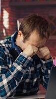 Tired man in living room home office shrugging head, upset after having to answer too many emails on laptop. Exhausted freelancer feeling overworked while typing on device keyboard, camera B video