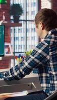 Man seated at desk using AI LLM chatbot software in modern urban home office. Person requesting help from large language model program on computer in bright apartment workspace, camera B video