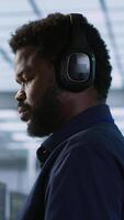 Vertical Computer scientist putting headphones on in server room, working to ensure minimal downtime. Engineer using audio device to hear podcasts in data center, monitoring performance, camera A video