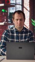 Employee completing spreadsheets on laptop and listening music. Worker in home office wearing headphones editing documents on notebook, updating reports and files, camera A video