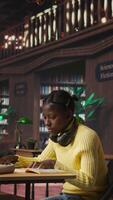 Vertical Portrait of cute teenager carrying textbooks and study materials in the library, preparing for a learning session to pass her exams. Young schoolgirl using books and academic resources. Camera A. video