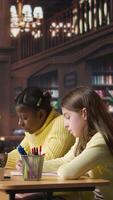 Vertical Diverse classmates scholars doing their class homework together in the library, working hard to obtain good grades. Focused schoolgirls solving their assignments with academic materials. Camera A. video