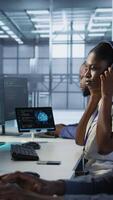 Vertical Engineer arrives in data center, puts headphones on, implementing AI systems. Server farm expert sitting down at desk, listening music and using artificial intelligence to prevent failures, camera A video