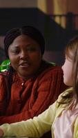 Vertical Elementary school pupils working with a professor practicing mathematics and developing their academic skills at a library desk. Black woman explains the curriculum materials. Camera B. video