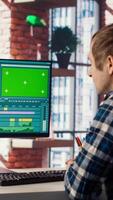 editor wearing headphones to polish footage and improve audio quality on green screen PC. Videographer professionally adjusting clips, applying sound effects using chroma key computer, camera B video